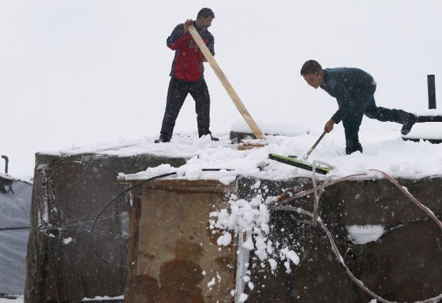 Syrian refugees remove snow from tents at a refugee camp during a wind storm in Zahle