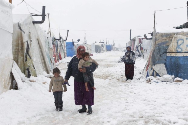 A Syrian refugee holds a barefoot child as she walks with a girl during snowfall at a refugee camp in Zahle